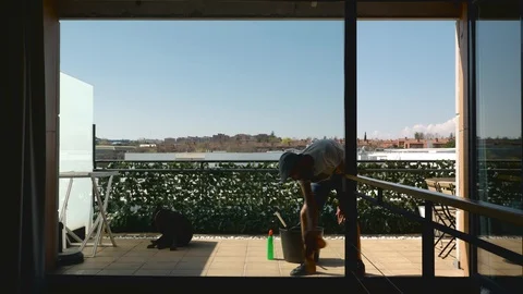 Middle-aged bearded man with his dog cleaning the windows of the terrace seen Stock Footage 127832597