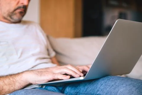 Middle-aged bearded man using laptop on sofa at home, selective focus on fi.. 스톡 사진