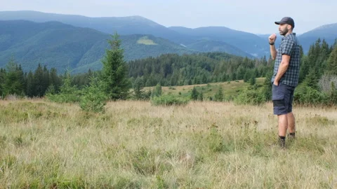 Middle-aged beared hiker man in plaid shirt is on the mountain glade and have a  Stock Footage 205608951