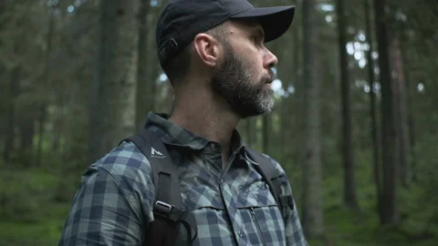 Middle-aged beared hiker man with backpack in a plaid shirt looks around in gree Video stock 208668981