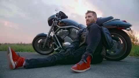 Middle-aged biker with beard sits by motorcycle at sunset Stock Footage 154915510