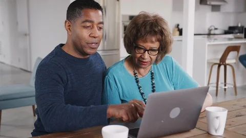 Middle aged black man helping his mother use a laptop computer at home, close up Stock Footage 106693861