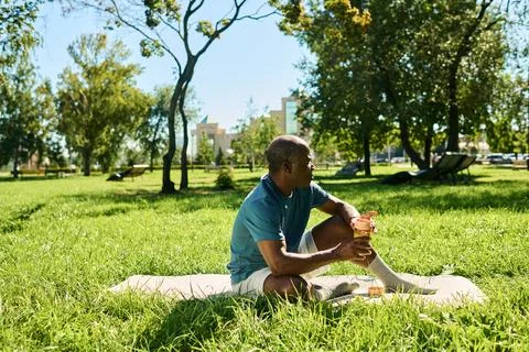 Middle Aged Black Man Resting on Mat in Sunny Park Foto stock
