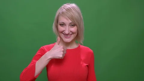 Middle-aged blonde short-haired model gestures thumb-up sign isolated on green Stock Footage 108679141