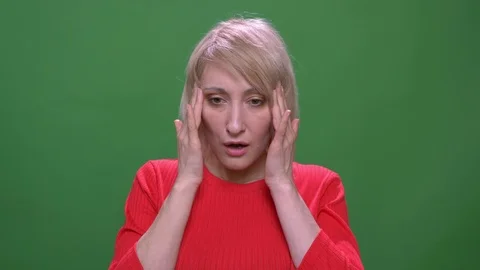 Middle-aged blonde short-haired model suffers from migraine isolated on green Stock Footage 108680224