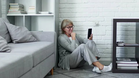 Middle Aged Blonde Sitting On The Floor In The Apartment And Talking On The 스톡 동영상 140942948