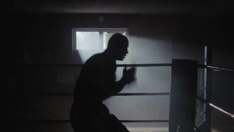 A middle aged boxer training in a dark gym with light coming from the window Stock Footage 258244538