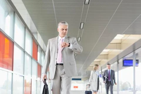 Middle aged businessman checking time with colleagues in background at railroad Stock Photos