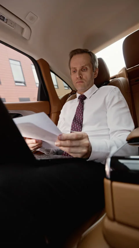 Middle Aged Businessman Reviewing Documents on Laptop in Luxury Car Stock Footage 339687091
