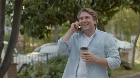Middle-aged businessman talking by cell phone in the park and drinking coffee. Stock Footage 140599332