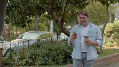Middle-aged businessman talking by cell phone in the park and drinking coffee. Video stock 140599576