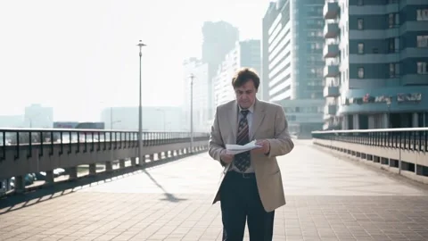 Middle-aged businessman walks down the street in the city, scans documents and Stock Footage 165383496