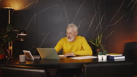 Middle-aged businessman working with documents and typing on a laptop in office 库存影片 340902498