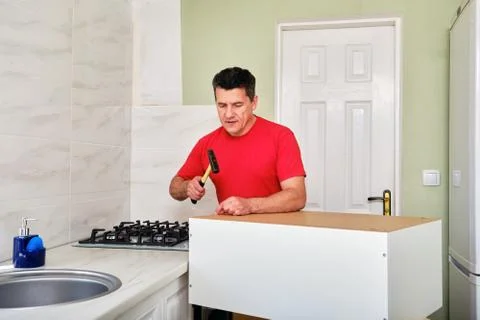 Middle aged caucasian man assembling kitchen cabinet with hammer and nails. Stock Photos