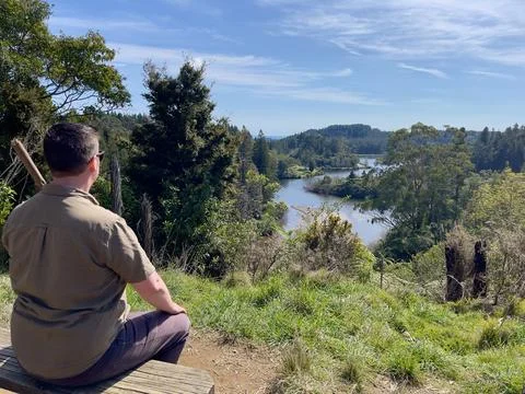Middle-aged caucasian man sits on a rustic wooden bench while holding a wooden w Stock Photos