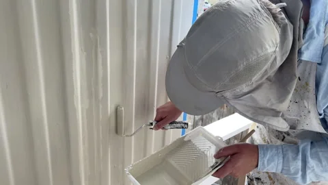 Middle-aged caucasian man in white painter's overalls uses a small paint roller  Stock Footage 275492637