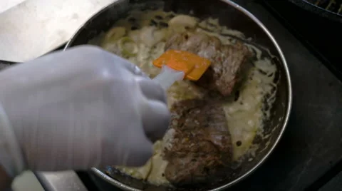 Middle aged chef mixing salsa of fried meat fillet with wooden spoon in a pan in Stock Footage 68562680