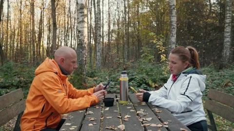 Middle-aged couple browsing smartphones, enjoying hot tea from thermos at wooden Vidéo 344342680