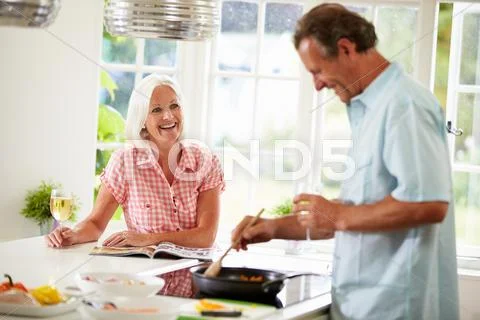 Middle aged couple cooking meal in kitchen together Stock Photos