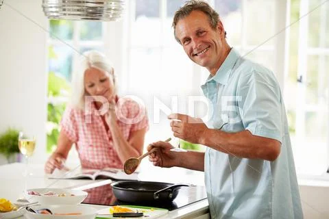 Middle aged couple cooking meal in kitchen together Stock Photos