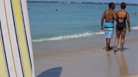 Middle-aged couple holding hands on a beach by a surfboard. Stock-Footage 88367868