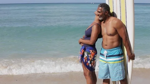 Middle-aged couple leaning on a surfboard on a beach. 스톡 동영상 88367541