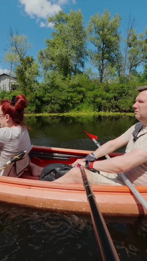 Middle aged couple paddling orange tandem kayak on river promoting active l.. Stock Footage 340211540
