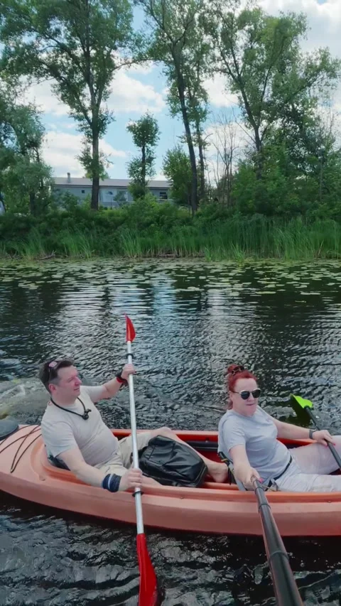 Middle-aged couple paddling orange tandem kayak on river promoting teamwork.. Stock Footage 345581841
