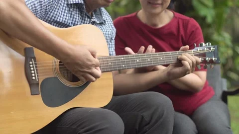 Middle aged  couple playing guitar while relax sitting on bench in backyard. Stock Footage 133410510