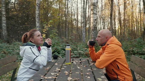 Middle-aged couple resting after walk enjoying hot tea from thermos at wooden pi Video stock 319606061