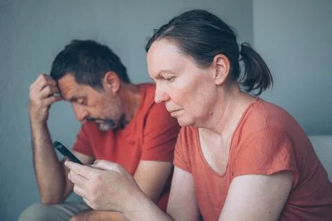 A middle-aged couple sit side by side, woman absorbed in her smartphones, i.. Stock Photos