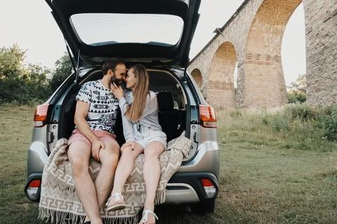 Middle-aged couple sitting inside trunk of SUV car with viaduct bridge on the Фото
