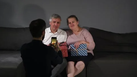 Middle-aged couple sitting on a sofa with gifts while their son takes a photo Video stock 340067107