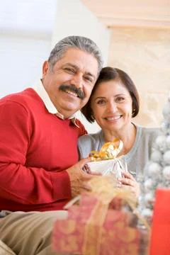 Middle Aged Couple Sitting On Sofa Holding Christmas Present Stock Photos