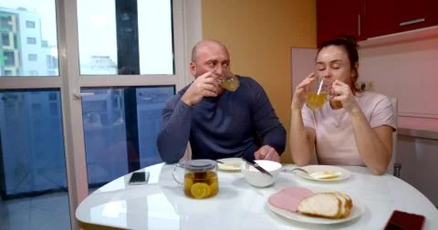 A middle-aged couple is sitting at a table in the kitchen by a large window Stock Photos