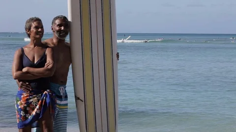Middle-aged couple by a surfboard on a beach. 스톡 동영상 88367468