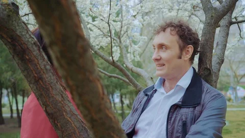 Middle-aged couple talking in the park,white flowering under the tree,they held Stock Footage 129473188