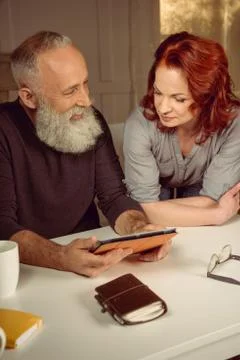 Middle aged couple using digital tablet while sitting at table at home Stock Photos