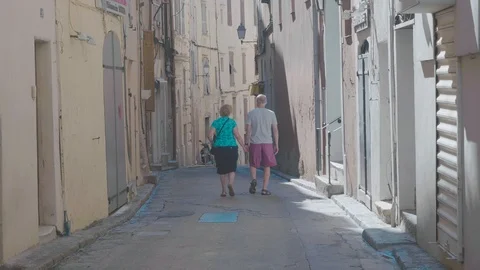 Middle aged couple walk down old street on a sunny holiday Stock Footage 88903474