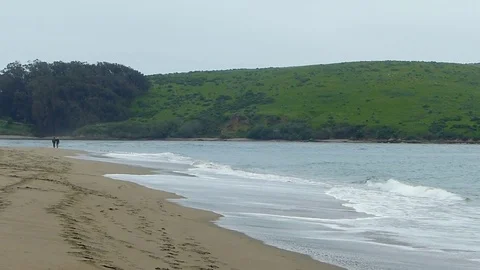 Middle aged couple walking along beach with green hills across water Stock Footage 75396705