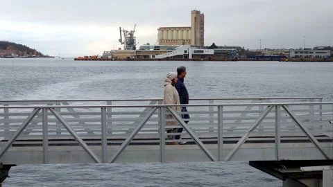 Middle-aged couple walking on bridge over water of lake or sea bay, silo and Stock Footage 231738643