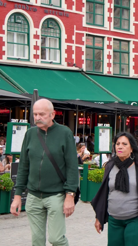 Middle-Aged Couple Walking Past Outdoor Cafes in Bruges Square Stock Footage 324685441