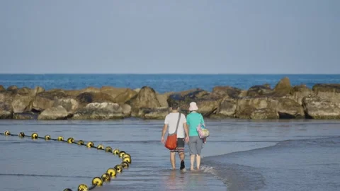Middle aged couple walking in shallow water in Tel Aviv beach in early morning Stock Footage 312446916