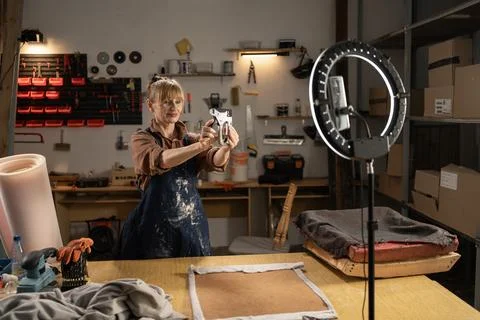 Middle aged craftswoman filming a tutorial about restoring furniture in her.. 스톡 사진