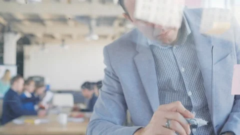 A middle-aged developer draws graphics on a glass board with a marker. Office Stock Footage 108979370