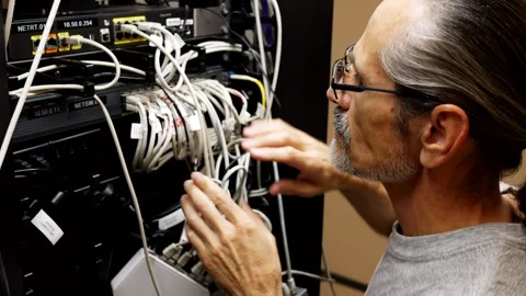 Middle-aged engineer with glasses in a server room connects network cables Stock Footage 247051839