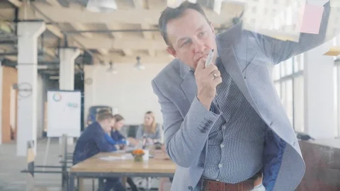 A middle aged engineer in a jacket thinks and draws graphics on a glass board Stock Footage 108981173