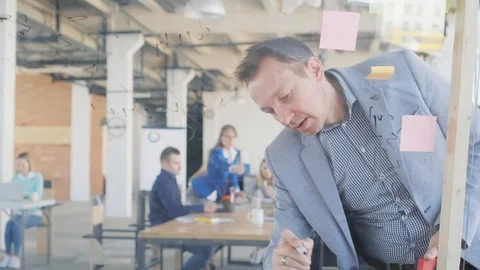 A middle-aged engineer writes formulas and graphs on a glass board using a Stock Footage 108979066