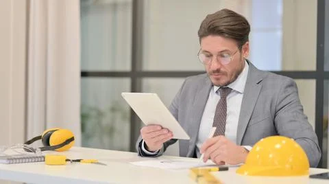 Middle Aged Engineer Writing Report while using Tablet in Office Stock Photos