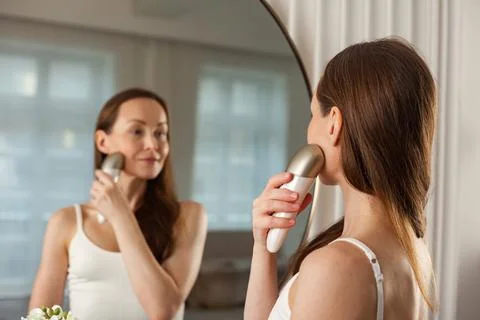 Middle aged female does led therapy facial massage using anti-aging electric  Stock-Fotos
